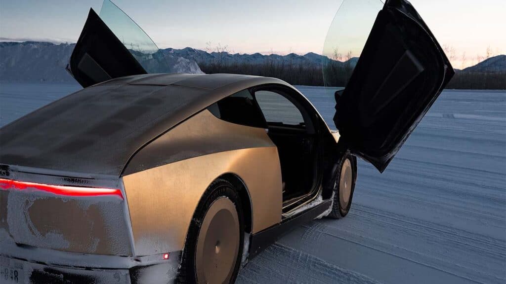 Coche eléctrico innovador con puertas abiertas en un paisaje nevado y montañoso al atardecer.
